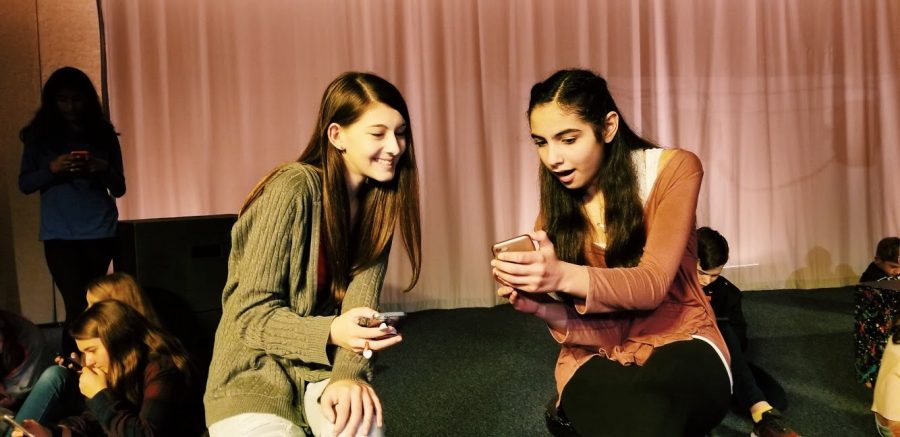 Hannah Moghaddar and Kira Hamburg act surprised as they look at a recent post during rehearsal for the fall play, Group Chat. 