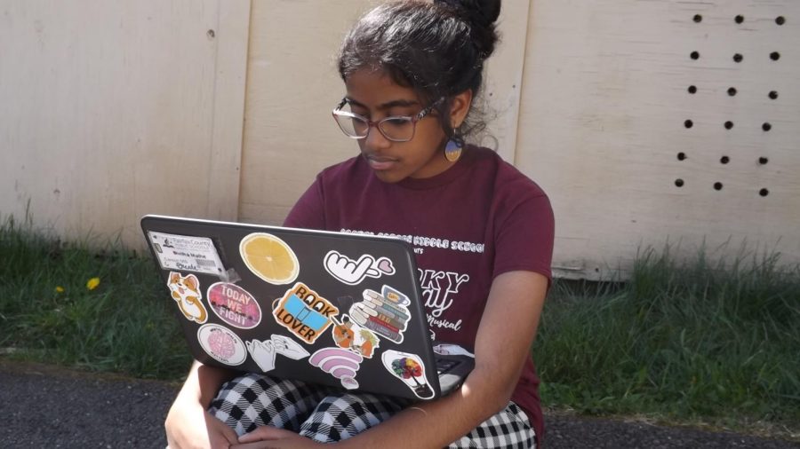                                     Divitha Mathe, an eighth- grader on the wolves team, is sitting outside by the      
                                                                       trailers while reading over her letter.
