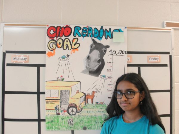 Bhavya Lavu, an eighth-grader on the discovery team, standing with her Panther time’s class poster, based on the book Animal Farm. 