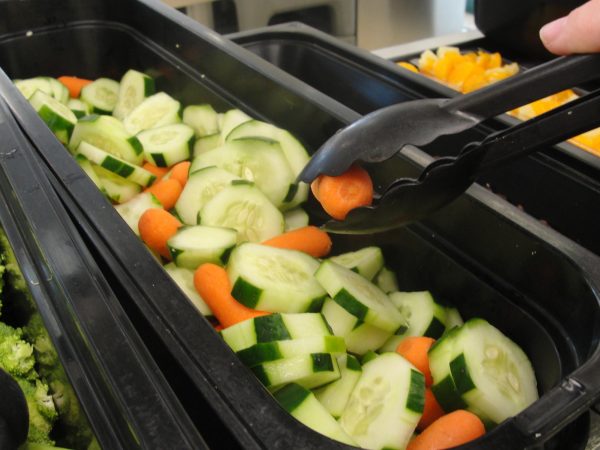 In a Cafeteria, an employee combines non-infected carrots and cucumbers in a carrot cucumber salad.